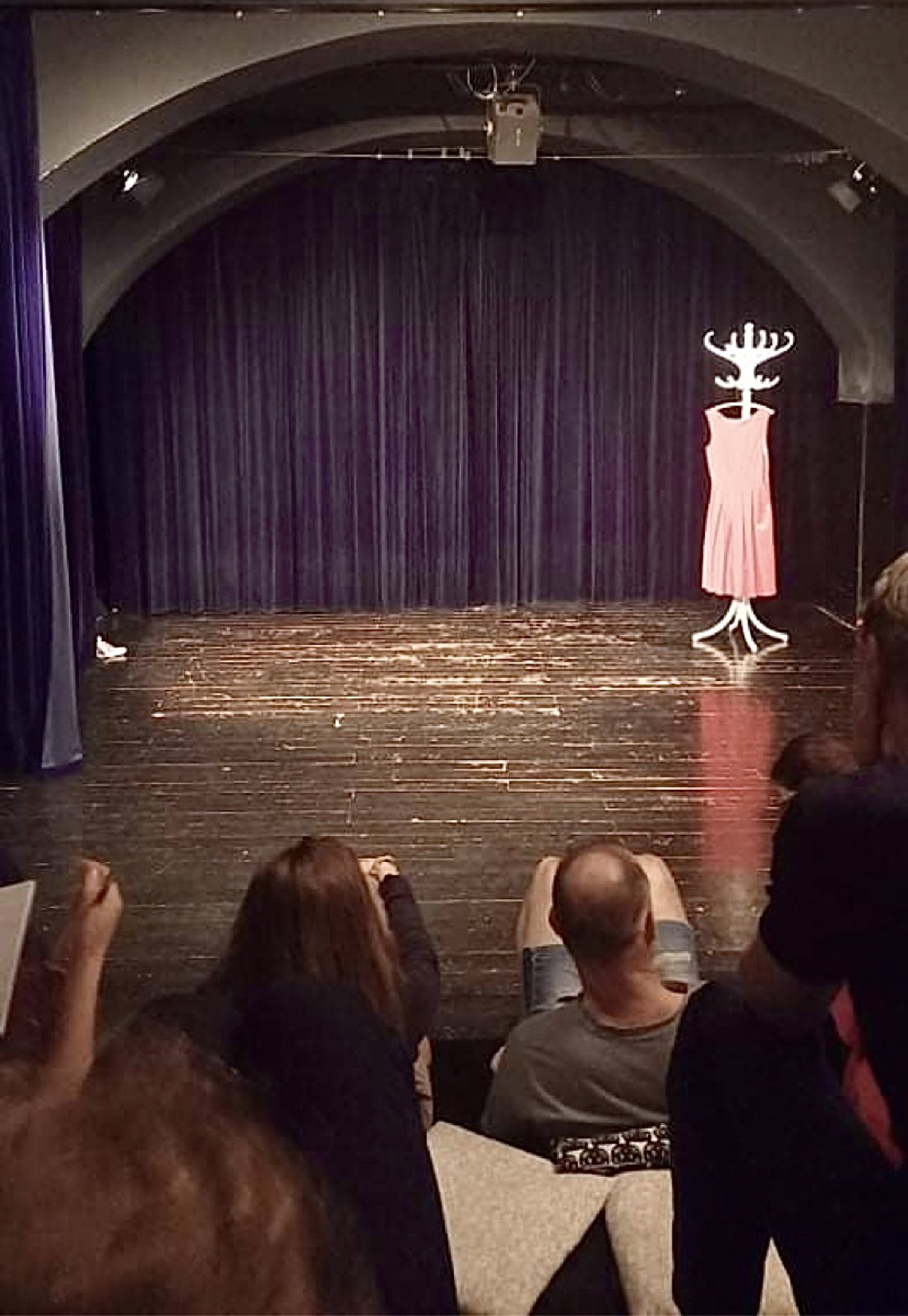 Escenario con un vestido rosa en un perchero, visto desde el público antes de cruzar el umbral